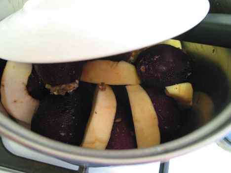 Stuffed eggplants and quince slices simmer on the stovetop under a heavy plate